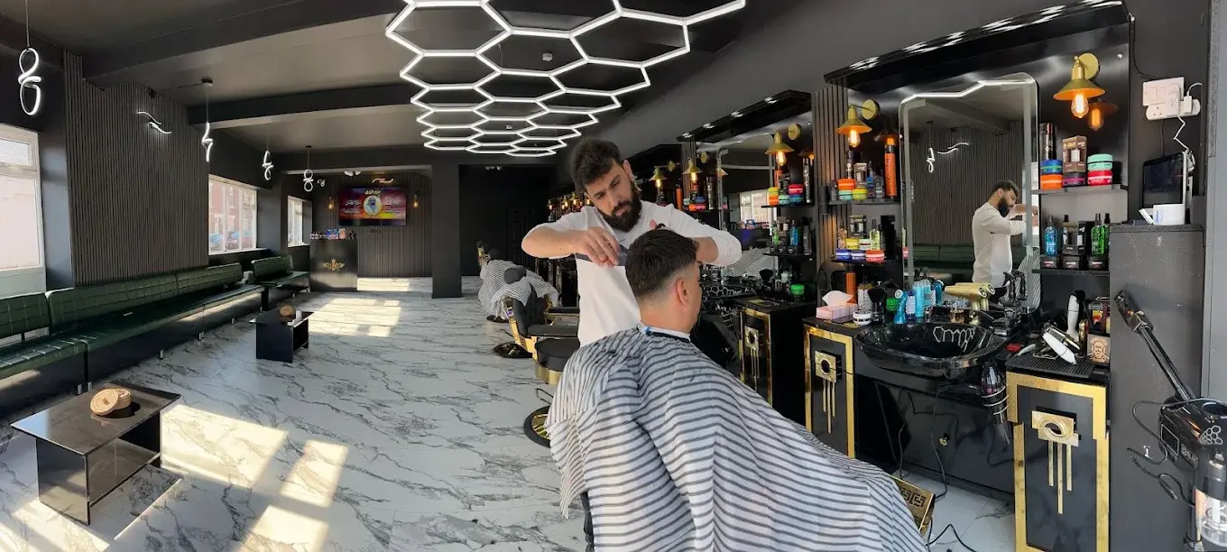 Wide view of the shop floor at HAWAR BARBER in Darlington: two barbers at work, a marble floor and green seating under the hexagon lights